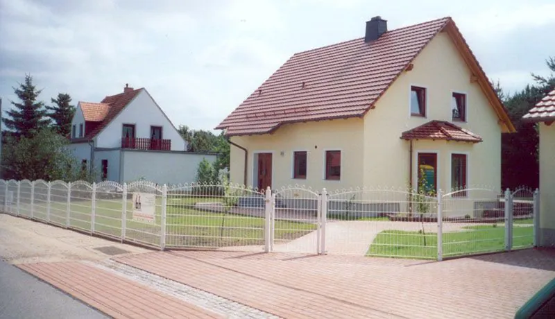Weißer Schmuckzaun mit Bogenfeldern und zweiflügeligem Tor vor einem Einfamilienhaus