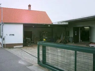 Werkstatthof mit offener Werkstatt und grünem Stabgitter-Schiebetor im Vordergrund