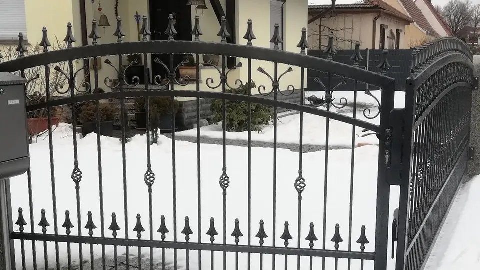 Schmiedeeiserne Pforte mit Bogen, Korbstäben und Lanzenspitzen vor einem verschneiten Vorgarten