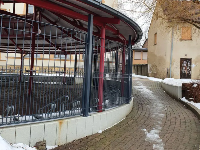 Doppelstabmattenzaun in Anthrazit, im Bogen um einen runden Fahrradunterstand vor einem historischen Schulgebäude